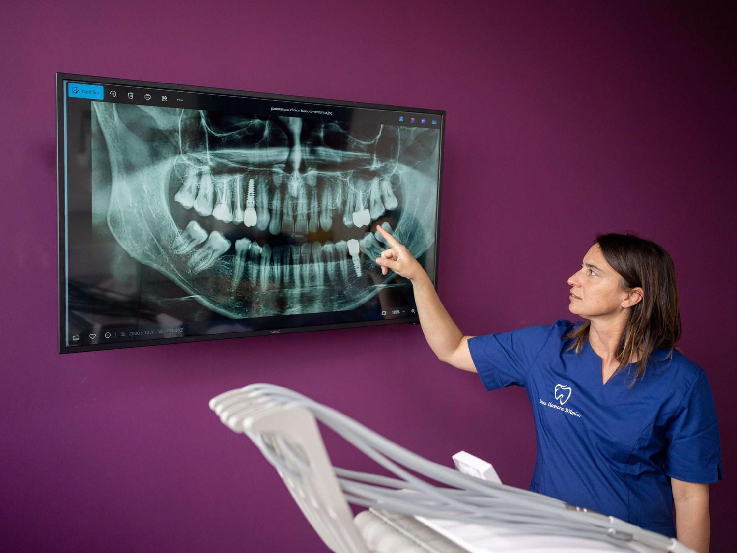 Una professionista dello studio indica una radiografia panoramica su un grande schermo, nella sala viola